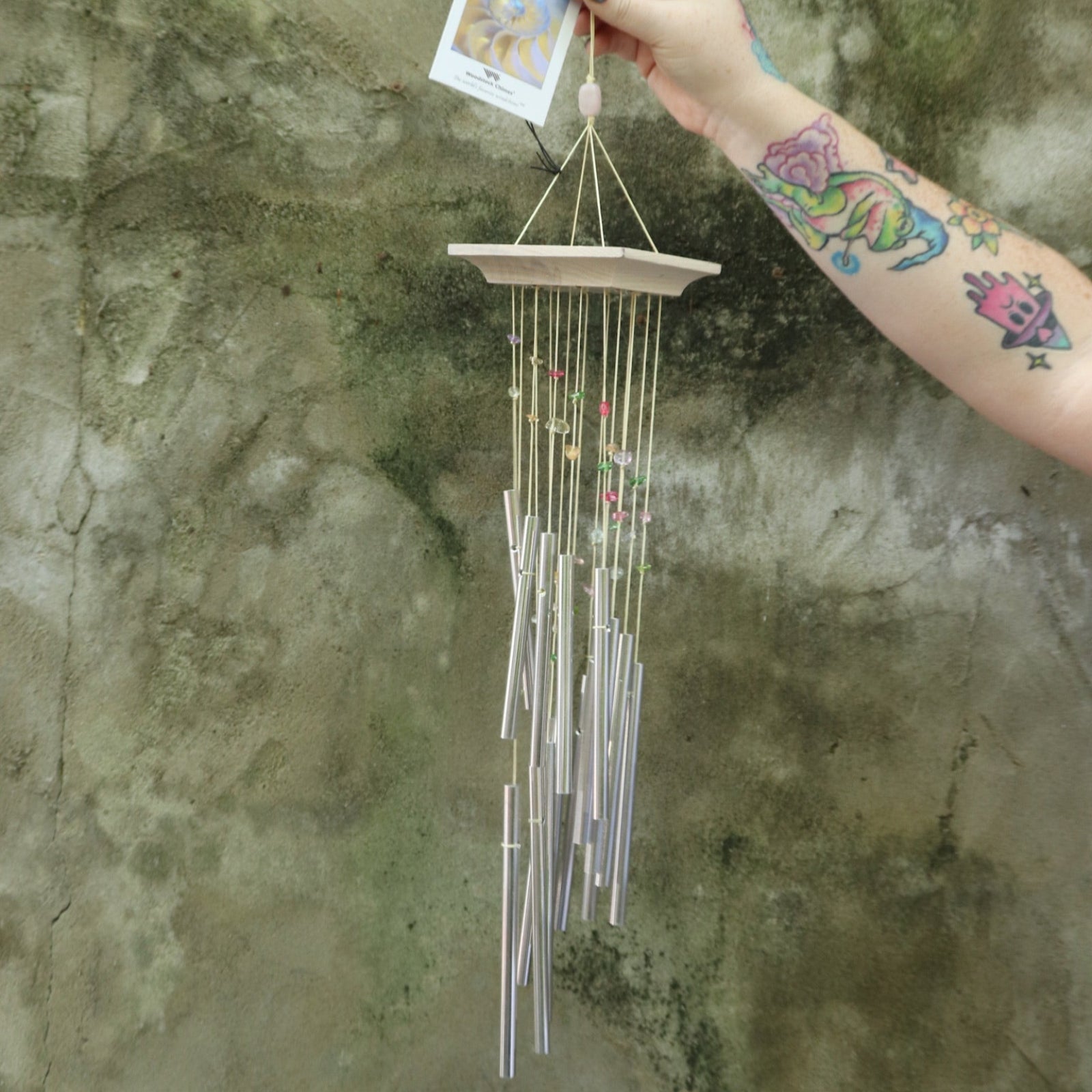Someone holding the Confetti Mystic Spiral Woodstock Wind Chime in front of a concrete wall.