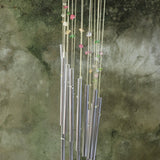 An up close image of someone holding the Confetti Mystic Spiral Woodstock Wind Chime in front of a concrete wall.