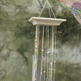 An up close image of someone holding the Confetti Mystic Spiral Woodstock Wind Chime in front of a concrete wall.