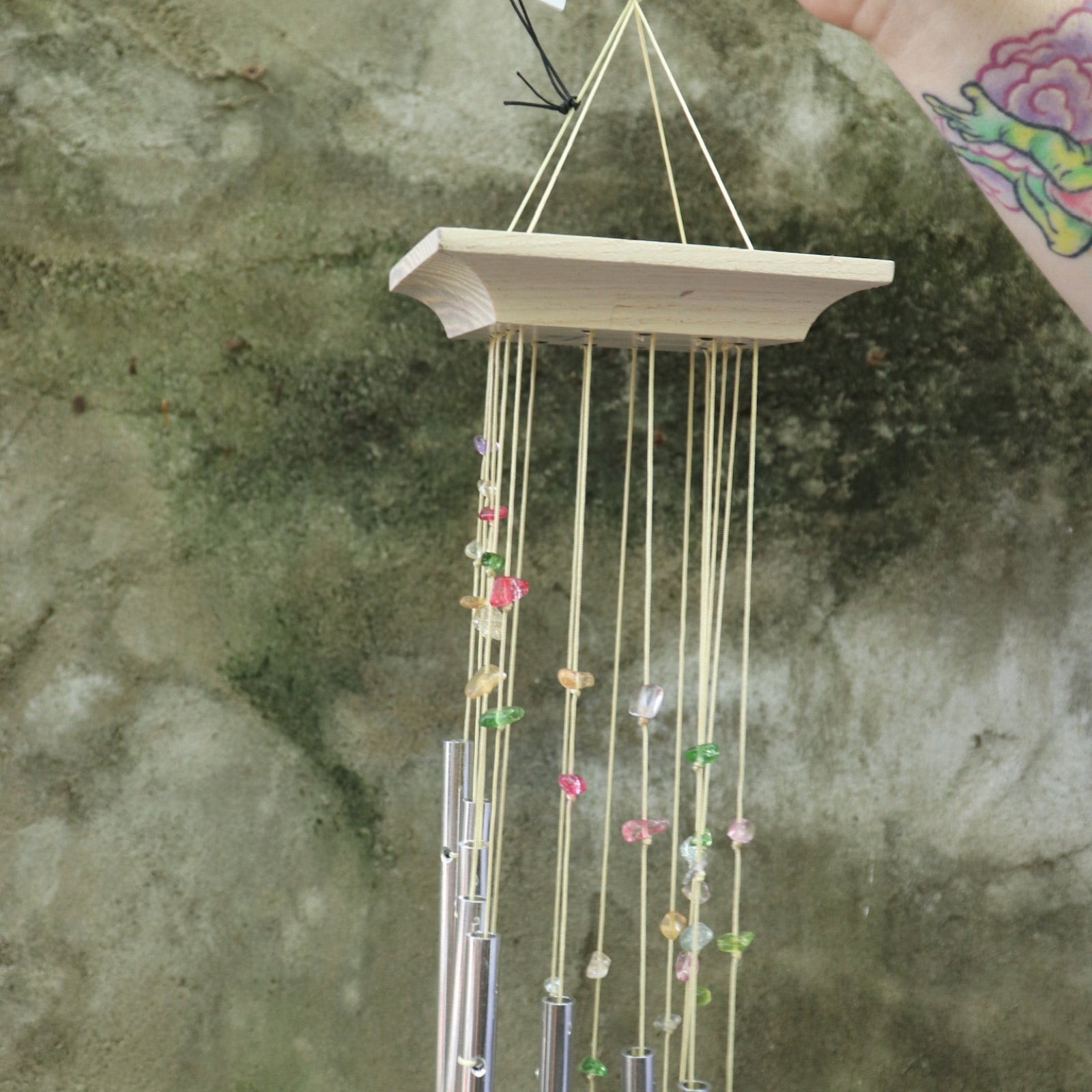 An up close image of someone holding the Confetti Mystic Spiral Woodstock Wind Chime in front of a concrete wall.