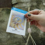 An up close image of someone holding the tag of the Confetti Mystic Spiral Woodstock Wind Chime in front of a concrete wall.