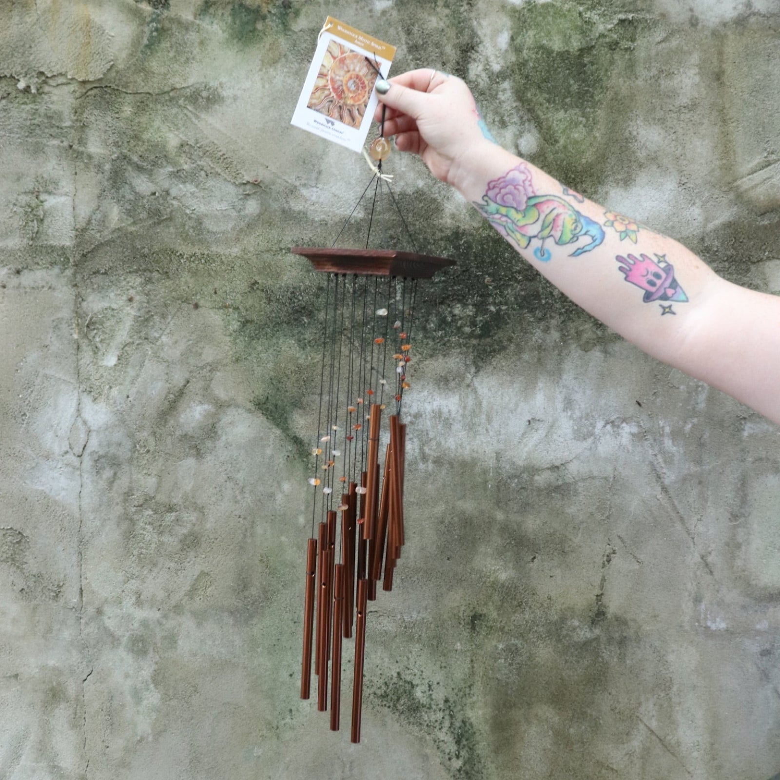 Someone holding the Amber Mystic Spiral Woodstock Wind Chime in front of a concrete wall.