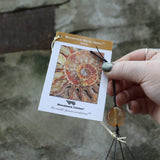 An up-close image of someone holding the tag of the Amber Mystic Spiral Woodstock Wind Chime in front of a concrete wall.
