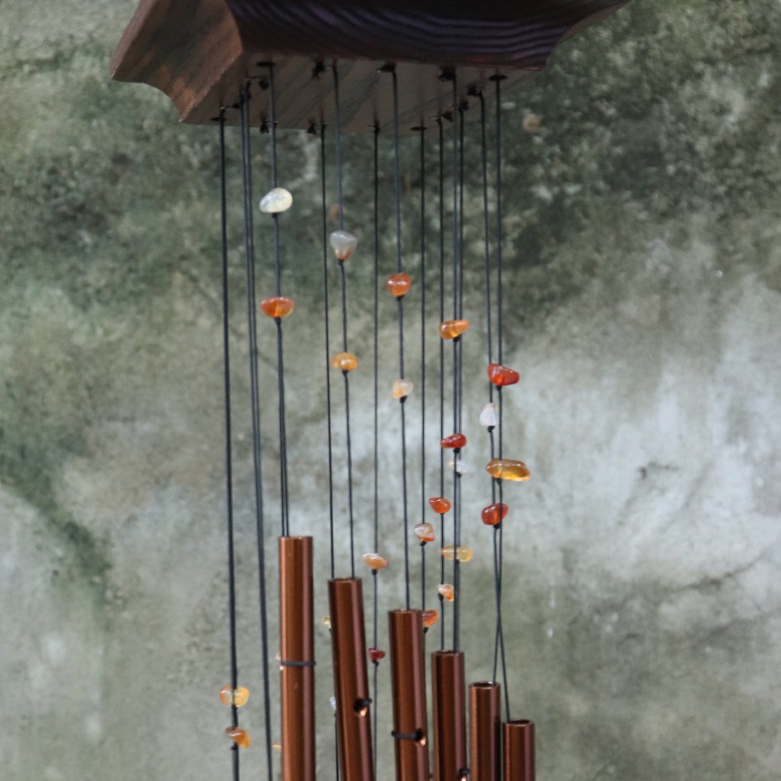 Someone holding the Amber Mystic Spiral Woodstock Wind Chime in front of a concrete wall.