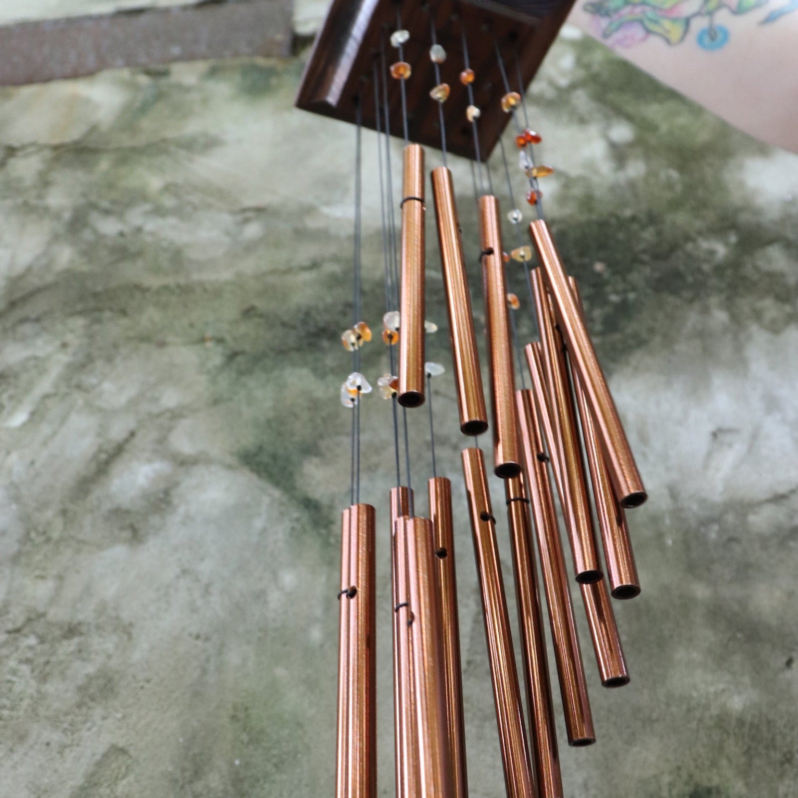Someone holding the Amber Mystic Spiral Woodstock Wind Chime in front of a concrete wall.