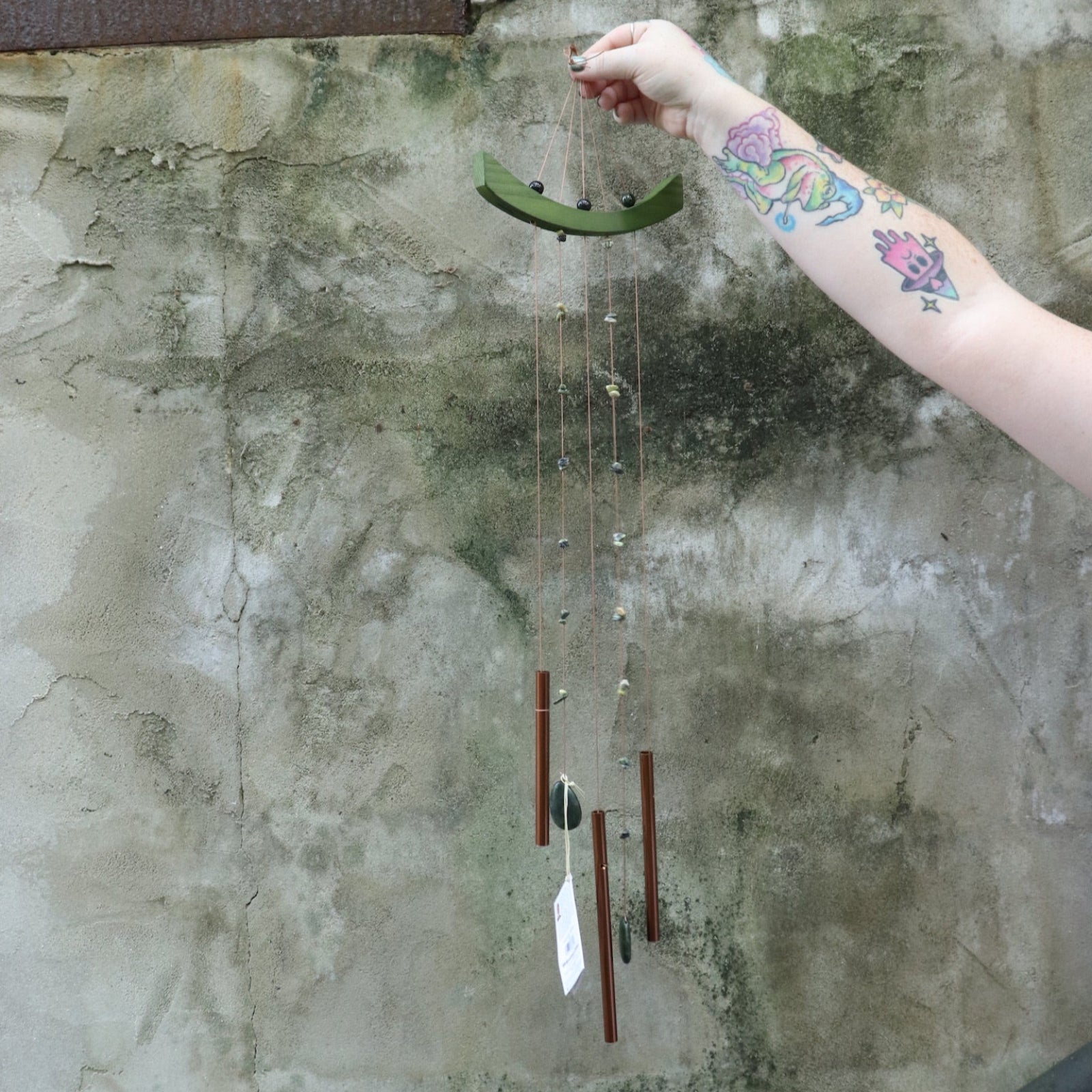 Someone holding the Small Jade Chi Energy Wind Chime in front of a concrete wall.
