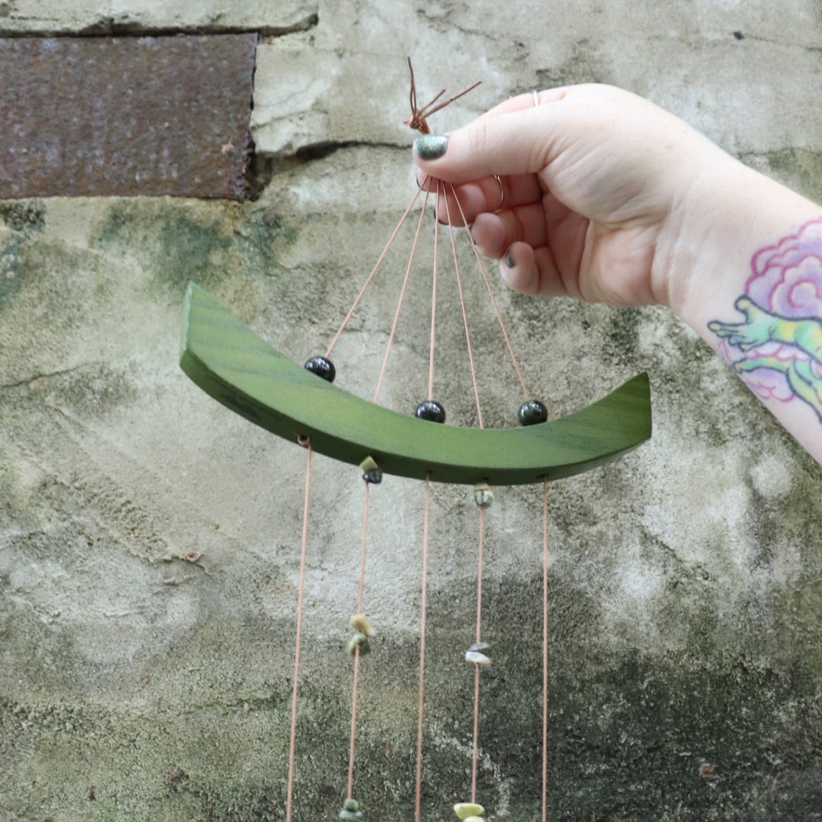 Someone holding the Small Jade Chi Energy Wind Chime in front of a concrete wall.