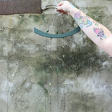Someone holding the Chi Energy Jade Feng Shui Woodstock Wind Chime in front of a cement wall.
