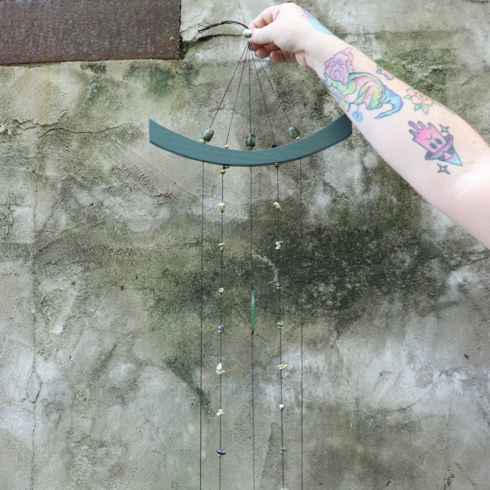 Someone holding the Chi Energy Jade Feng Shui Woodstock Wind Chime in front of a cement wall.