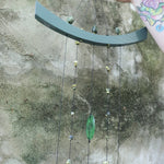 Someone holding the Chi Energy Jade Feng Shui Woodstock Wind Chime in front of a cement wall.