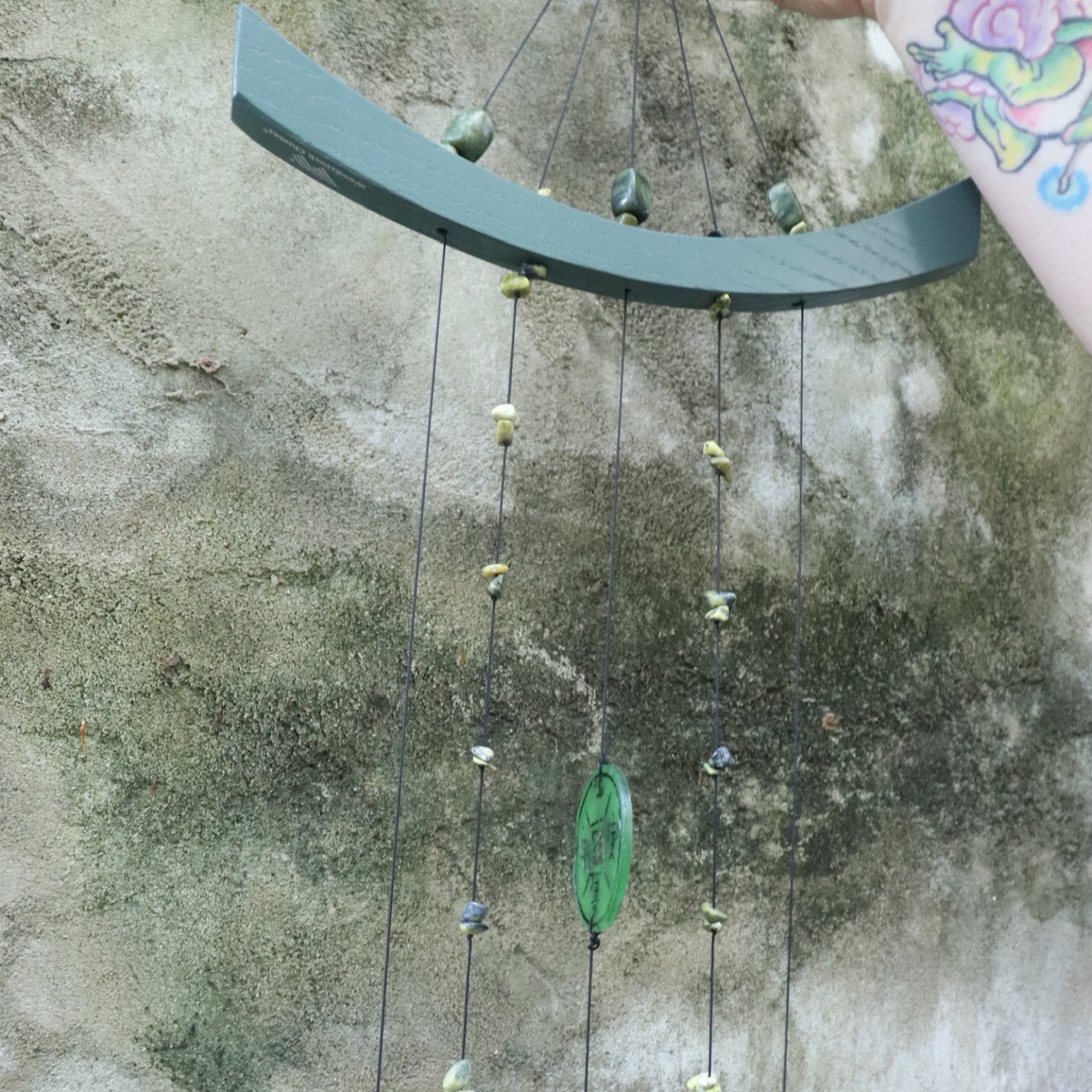 Someone holding the Chi Energy Jade Feng Shui Woodstock Wind Chime in front of a cement wall.