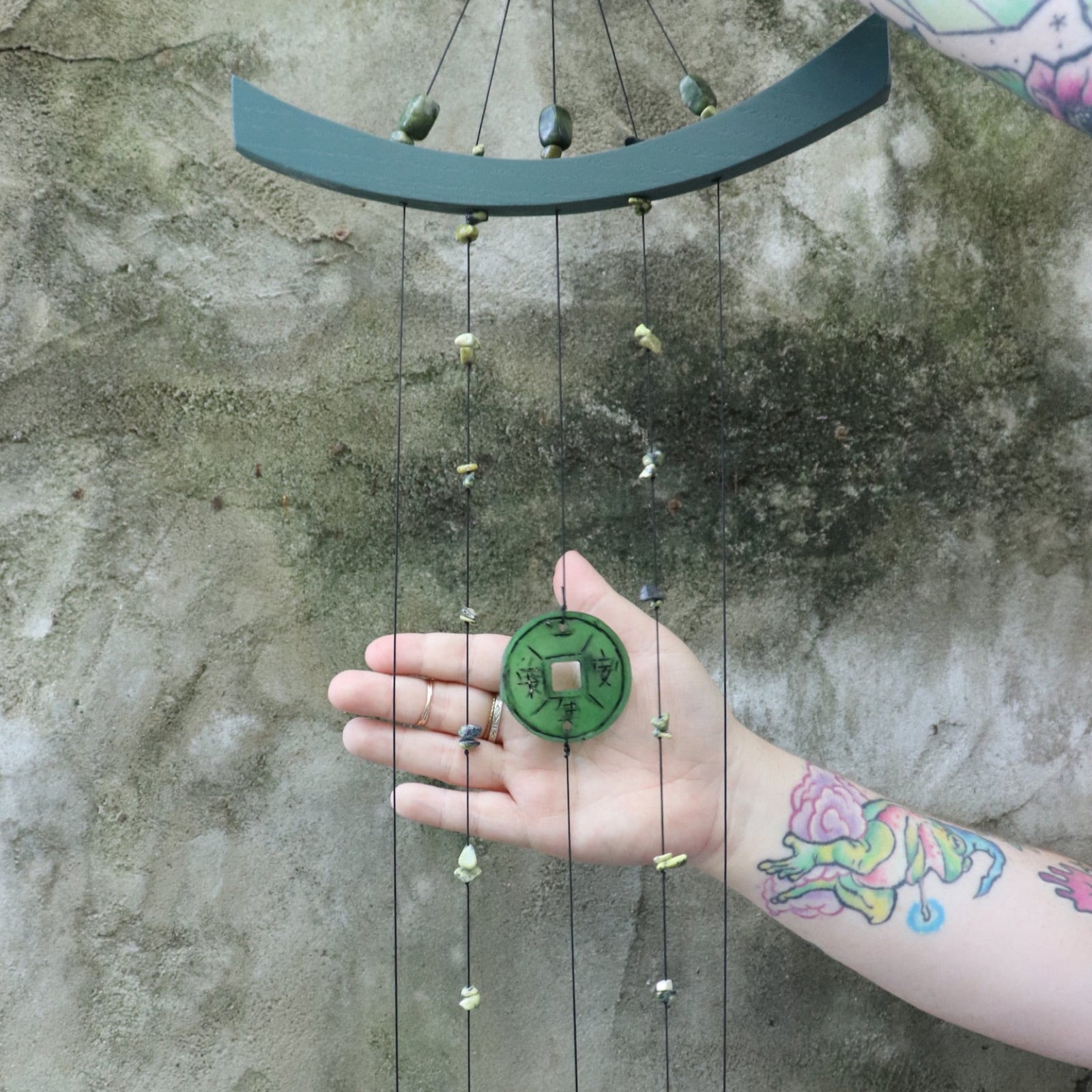 Someone holding the Chi Energy Jade Feng Shui Woodstock Wind Chime in front of a cement wall.