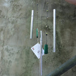 Someone holding the Chi Energy Jade Feng Shui Woodstock Wind Chime in front of a cement wall.