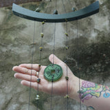 Someone holding the Chi Energy Jade Feng Shui Woodstock Wind Chime in front of a cement wall.