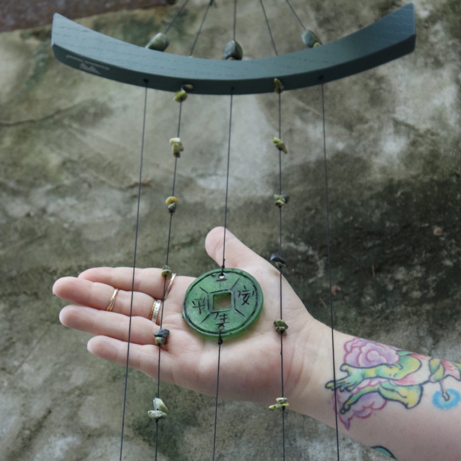 Someone holding the Chi Energy Jade Feng Shui Woodstock Wind Chime in front of a cement wall.