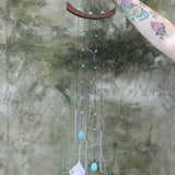 Someone holding the Small Turquoise Chi Energy Wind Chime in front of a cement wall.