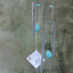 An up-close image of someone holding the Small Turquoise Chi Energy Wind Chime in front of a cement wall.