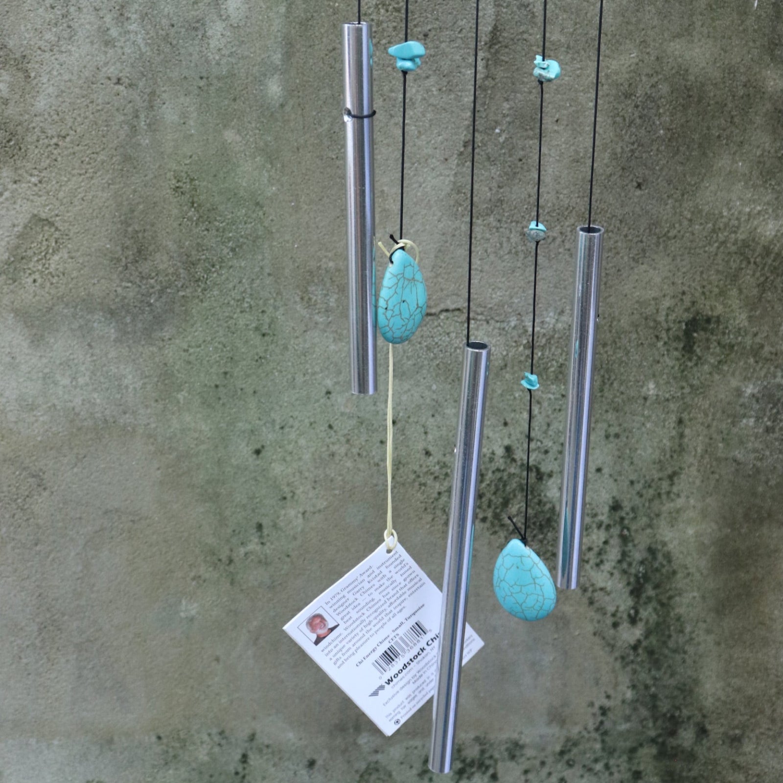 An up-close image of someone holding the Small Turquoise Chi Energy Wind Chime in front of a cement wall.