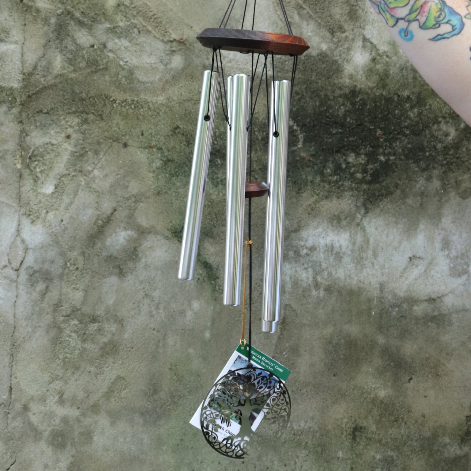 Someone holding the Mirror Tree of Life Woodstock Habitats Wind Chime in front of a cement wall.