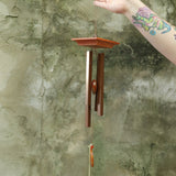Someone holding the Woodstock Amber Wind Chime in front of a cement wall .