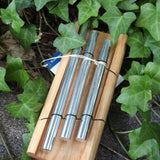 The Woodstock Zenergy Trio Chime on a dark cement background surrounded by ivy.
