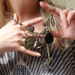 A woman wearing the Gypsy Junk Original-Gray 24" Necklace and holding it up to show individual charms.