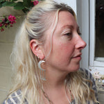 A woman wearing the Silver Many Moons 2.5 inch. Earrings.