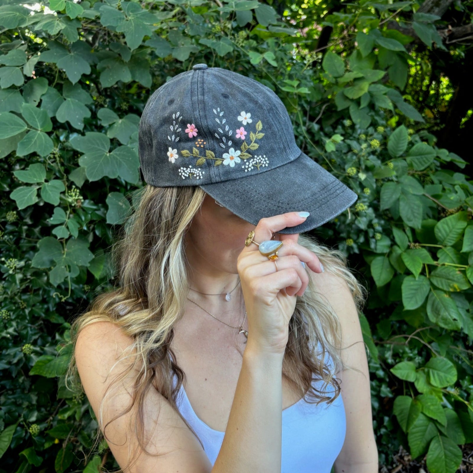 A woman wearing the Flower Garden Embroidered Adjustable Baseball Cap in front of greenery.