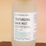 An up close image of the Patchouli Vanilla Sea Salt Texturizing Hair Mist by Bohemian Rêves on an agate slice all on a pink and yellow background.