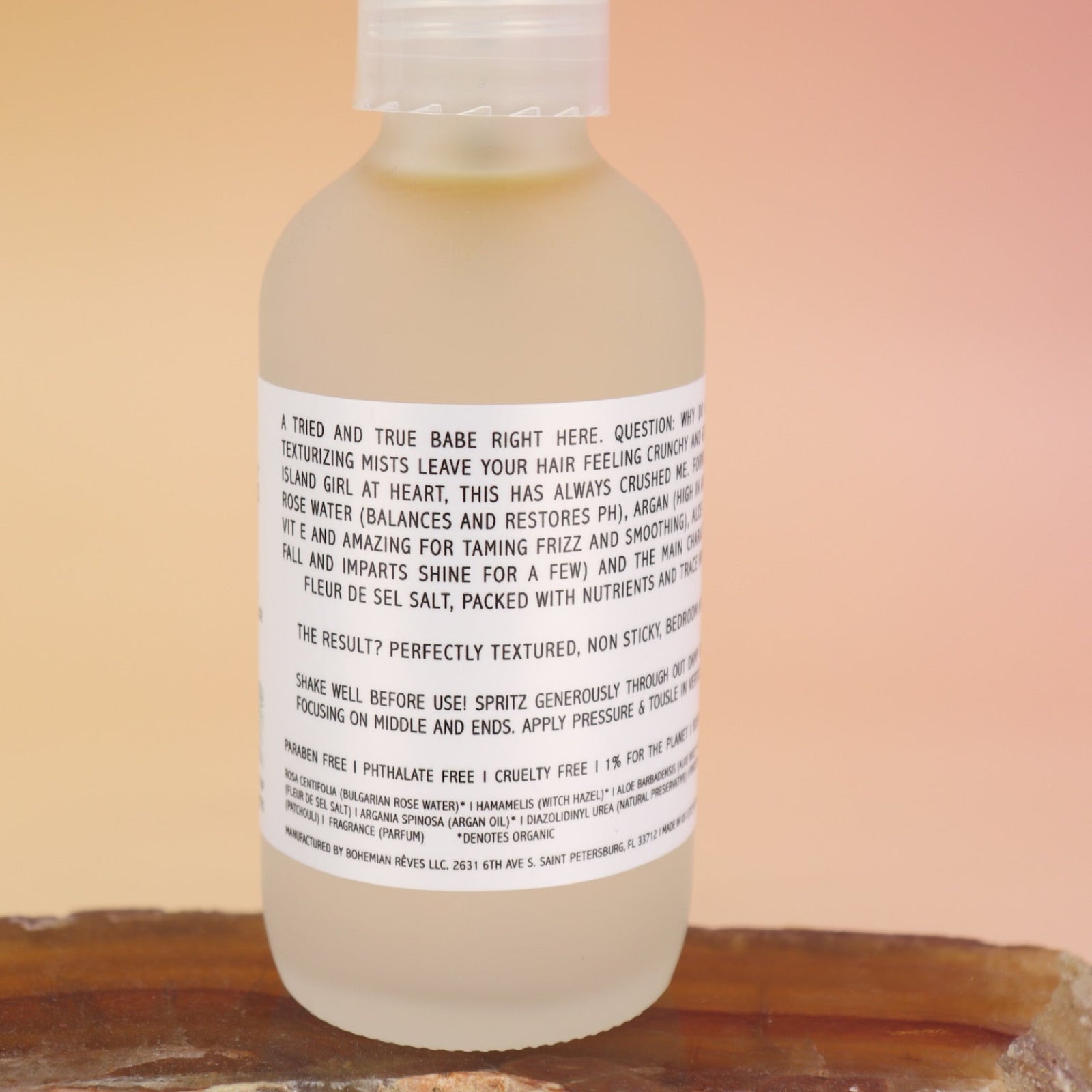 An up close image of the back of the Patchouli Vanilla Sea Salt Texturizing Hair Mist by Bohemian Rêves on an agate slice all on a pink and yellow background.