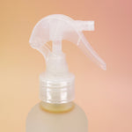 An up close image of the Patchouli Vanilla Sea Salt Texturizing Hair Mist and its pump on a pink and yellow background.