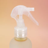 An up close image of the Patchouli Vanilla Sea Salt Texturizing Hair Mist and its pump on a pink and yellow background.