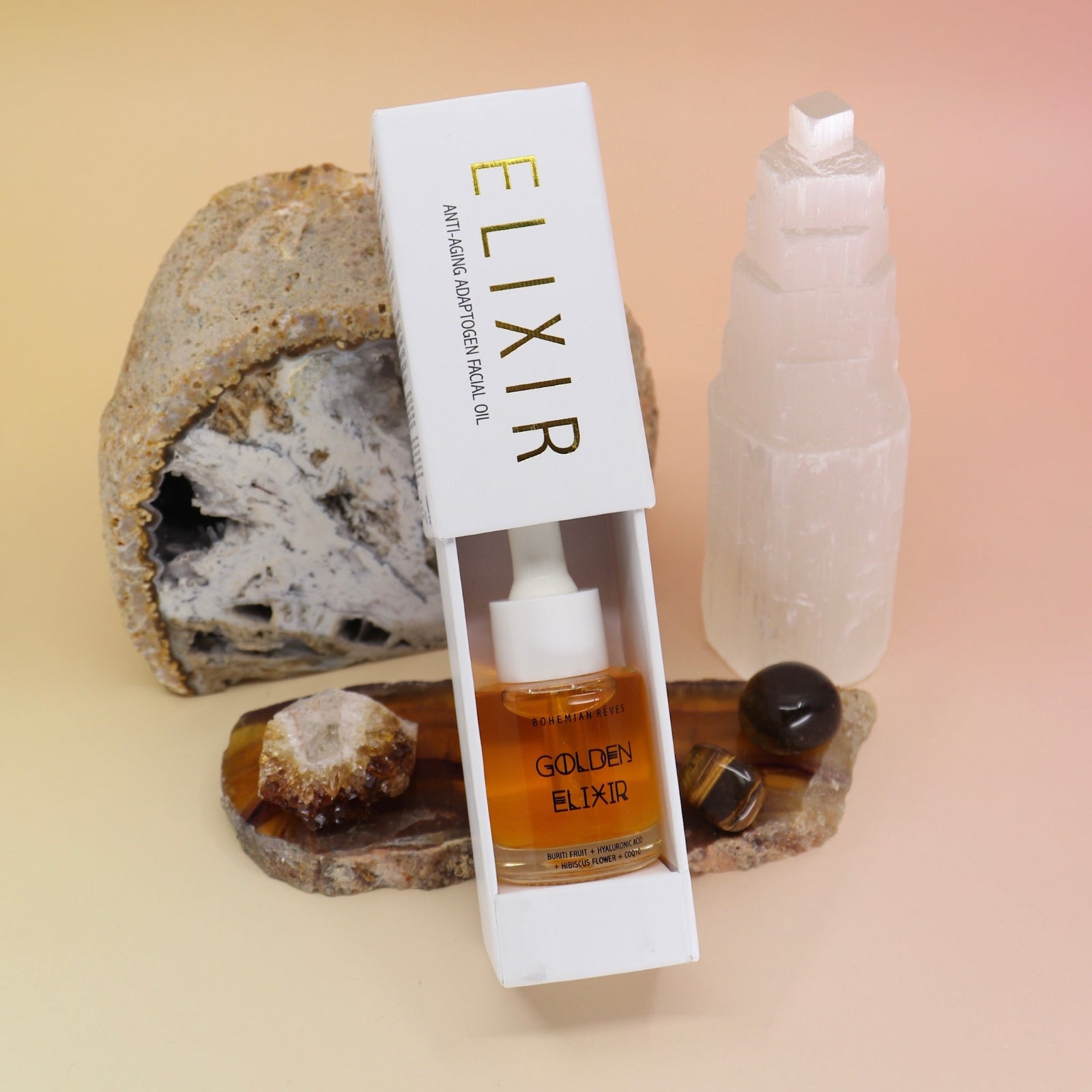 The Anti-Aging Elixir Face Oil from Bohemian Rêves on a slice of agate in front of a open geode and selenite tower, all on a pink and yellow background.