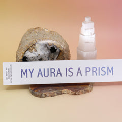 The My Aura Is A Prism Hand-Rolled Incense Sticks Package on a agate slice in front of an open geode and a selenite tower all on a pink and yellow background.