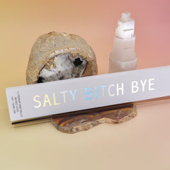 The Bohemian Rêves - Salty Bitch Bye Hand Rolled Botanical Incense Sticks on an agate slice in front of an open geode and a selenite tower all on a pink and yellow background.