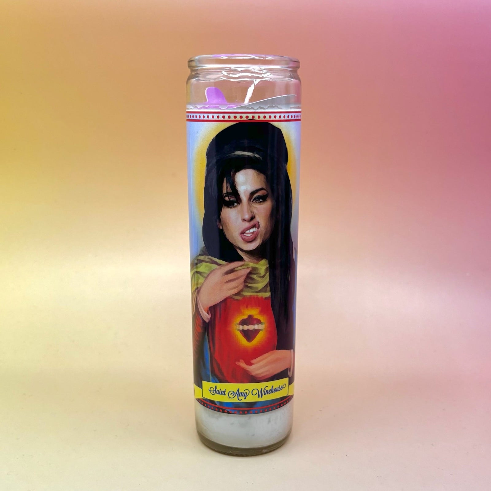 The Saint Amy Winehouse Devotional Prayer Candle in front of a pink and yellow background.