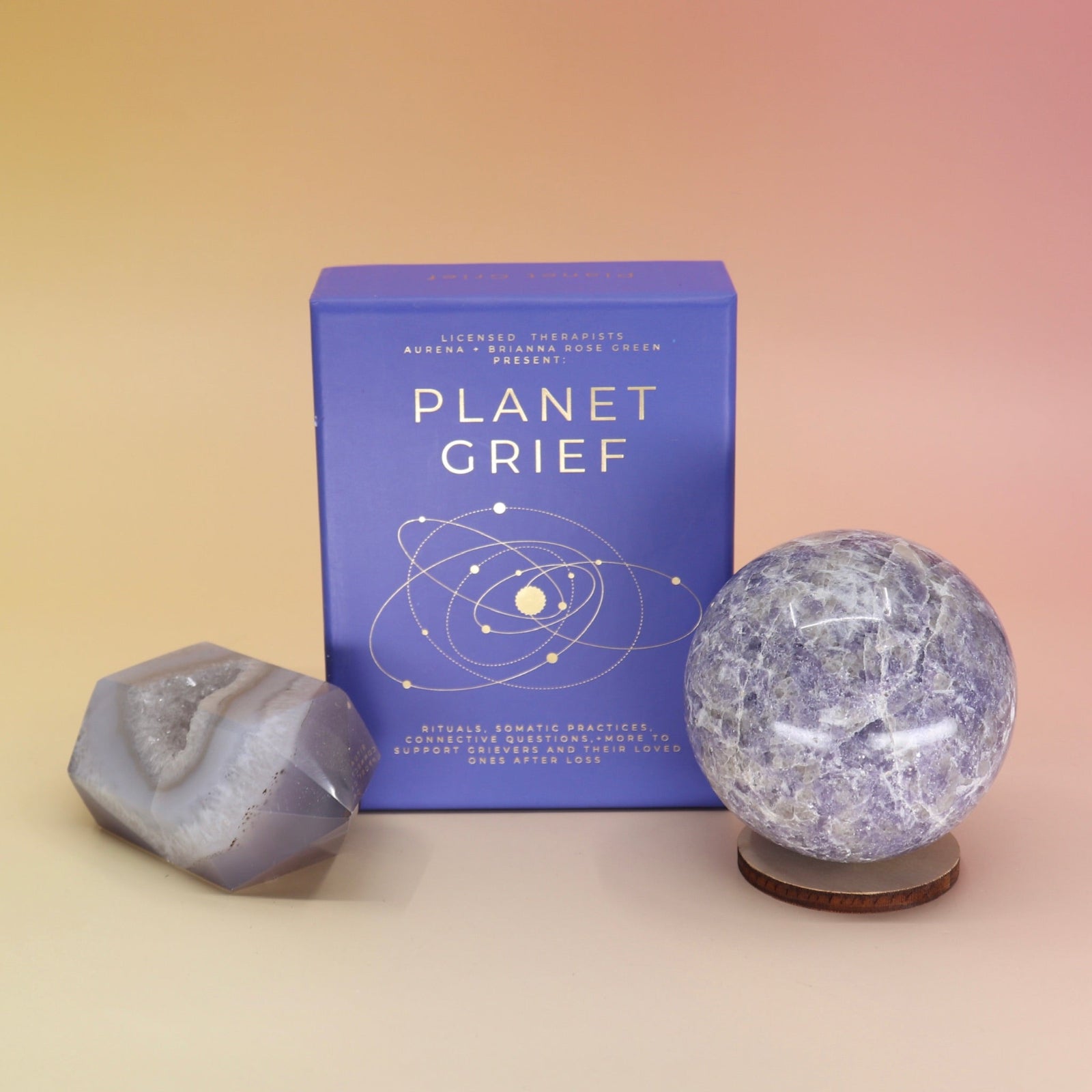 The Planet Grief Card Deck Bereavement Resource on a pink and yellow background, with two crystals in front of it.