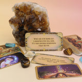 The contents of the Magical Messages from the Universe Affirmation + Divination Cards leaning against a citrine piece all on a pink and yellow background.