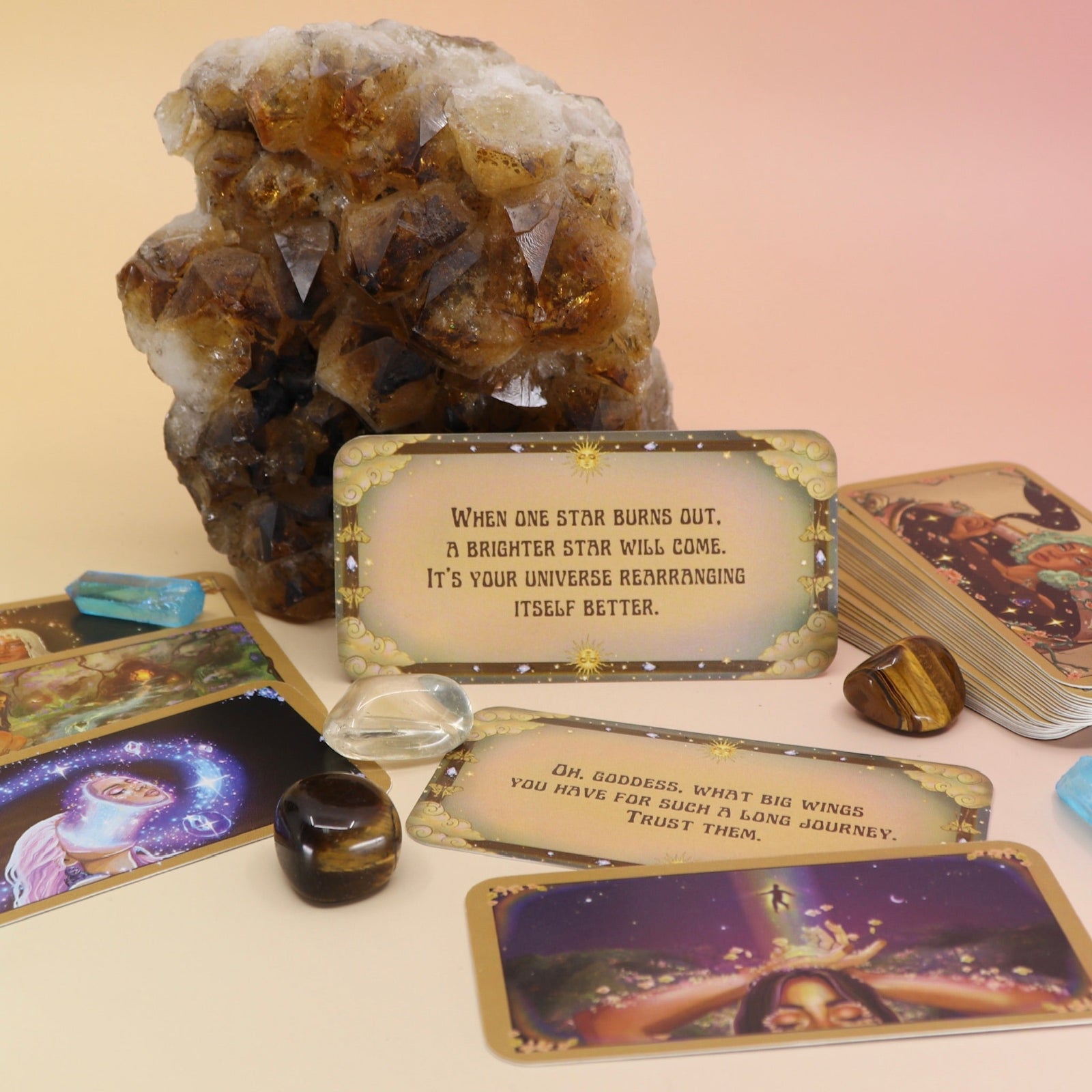 The contents of the Magical Messages from the Universe Affirmation + Divination Cards leaning against a citrine piece all on a pink and yellow background.
