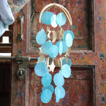 Someone holding the Moon & Stars Capiz Chime in front of a wooden door.