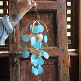 Someone holding the Moon & Stars Capiz Chime in front of a wooden door.