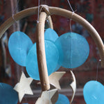 An up-close image of the chapiz, coconut accents, and arched rattan top within the Moon & Stars Capiz Chime.