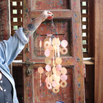 Someone holding the Sunlit Bay Capiz Chime in front of a door.