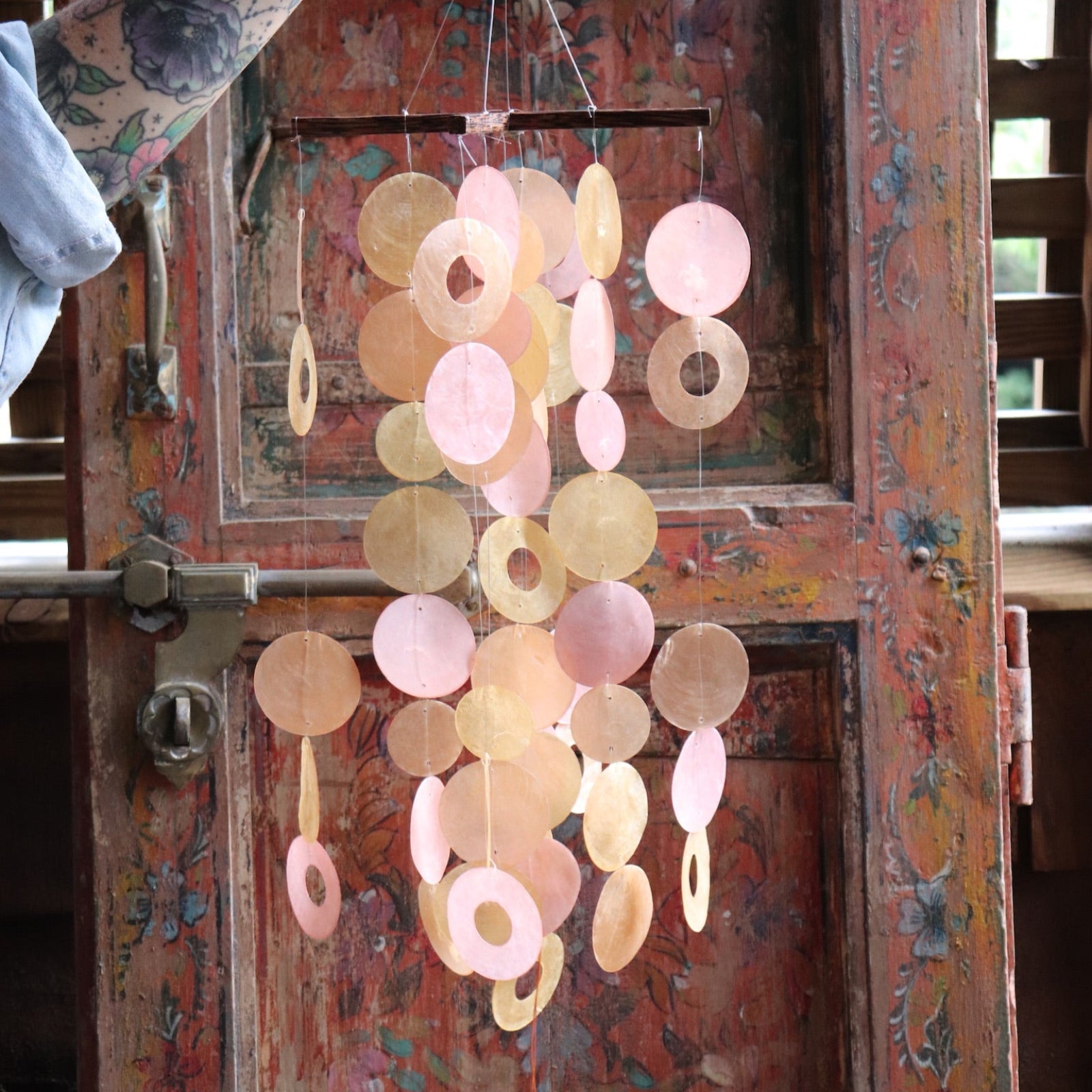 Someone holding the Sunlit Bay Capiz Chime in front of a door.