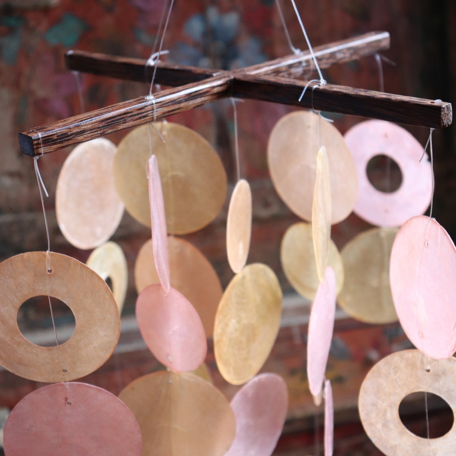An up-close image of the Sunlit Bay Capiz Chime in front of a door.