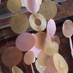 An up-close image of the Sunlit Bay Capiz Chime in front of a door.