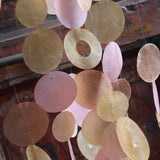 An up-close image of the Sunlit Bay Capiz Chime in front of a door.