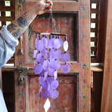 Someone holding the Purple Capiz Chime in front of a wooden door.