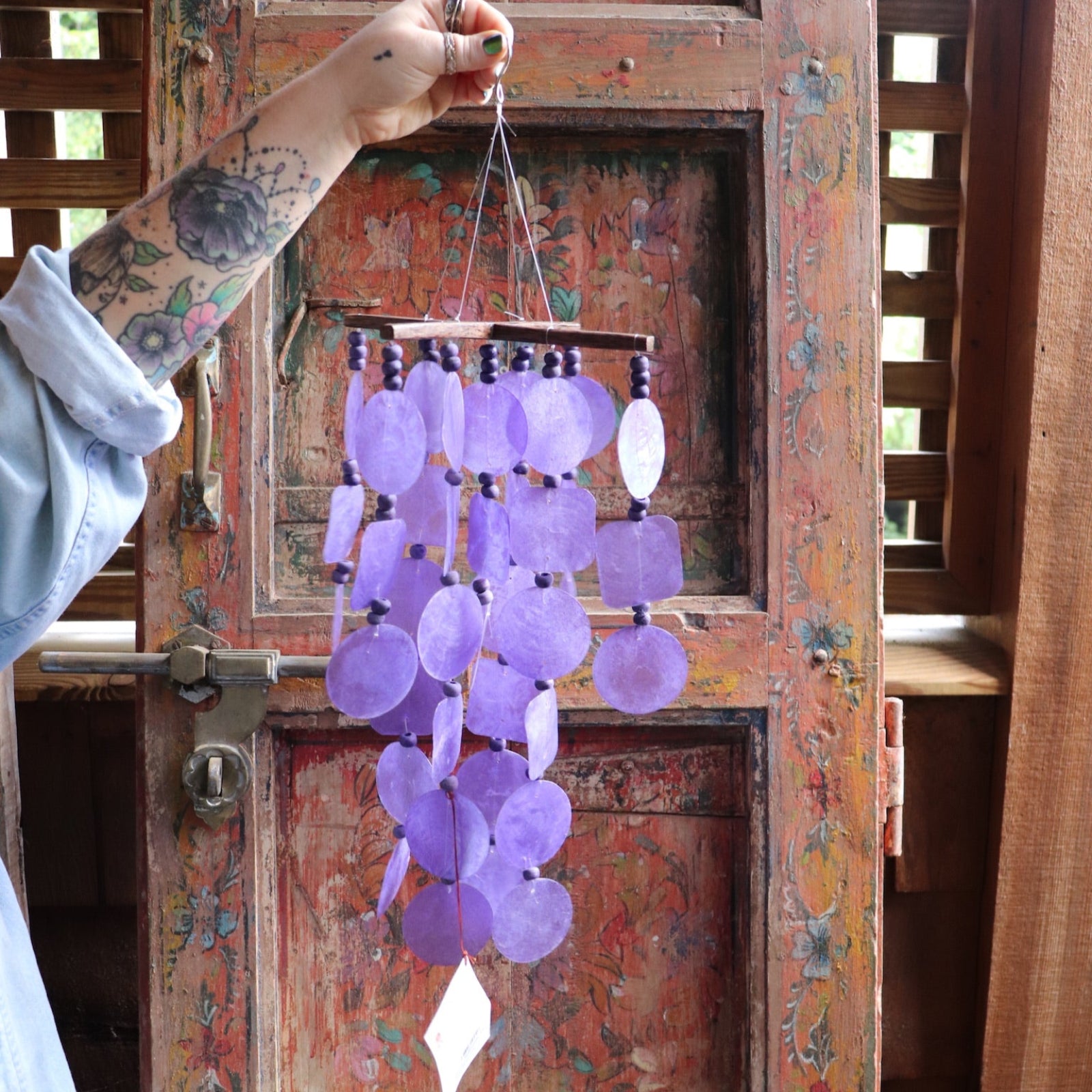 Someone holding the Purple Capiz Chime in front of a wooden door.