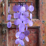 Someone holding the Purple Capiz Chime in front of a wooden door.